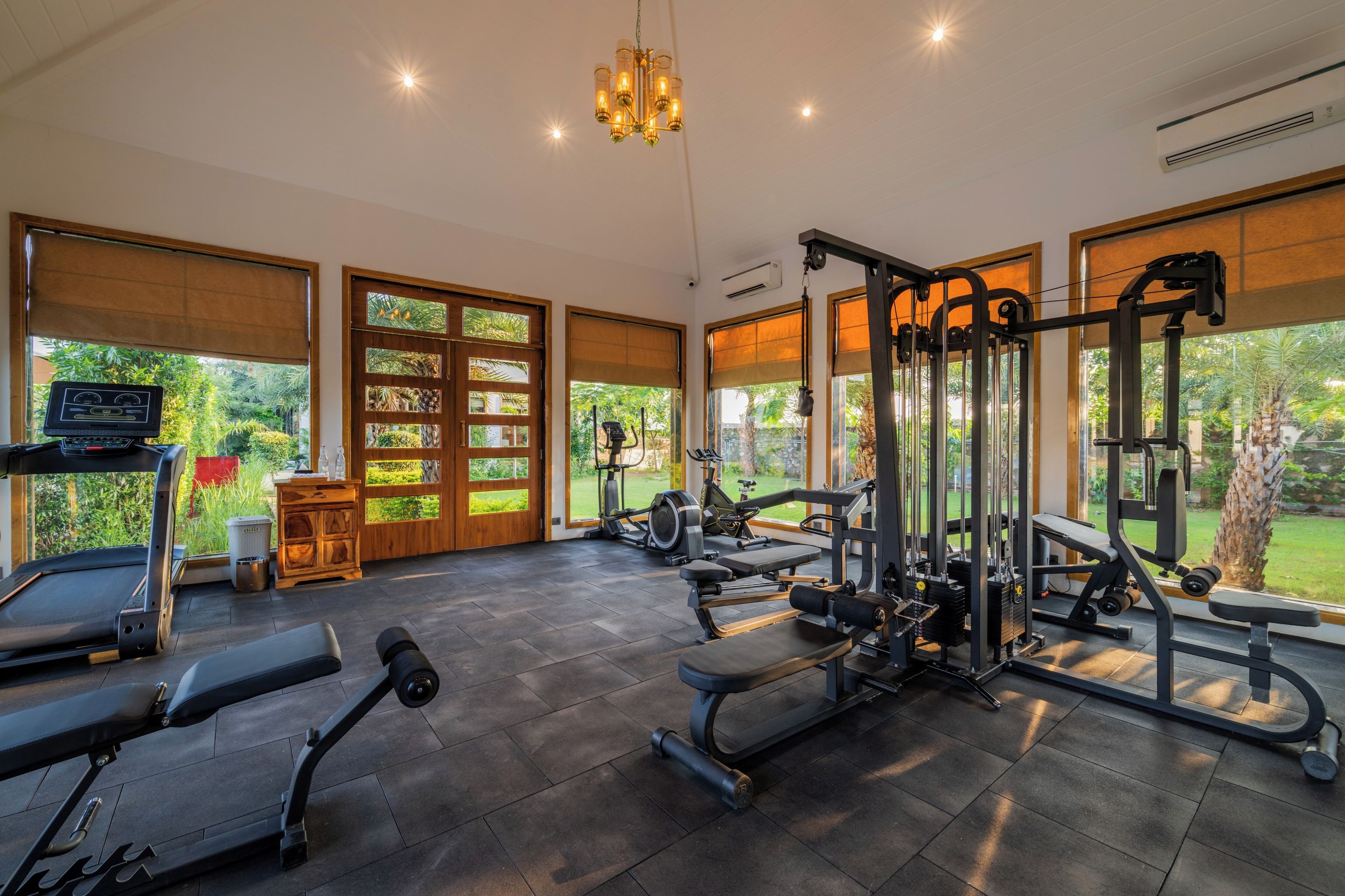 Une salle de sport spacieuse, dotée de divers appareils d’exercice, de grandes fenêtres et offrant une vue sur la verdure.