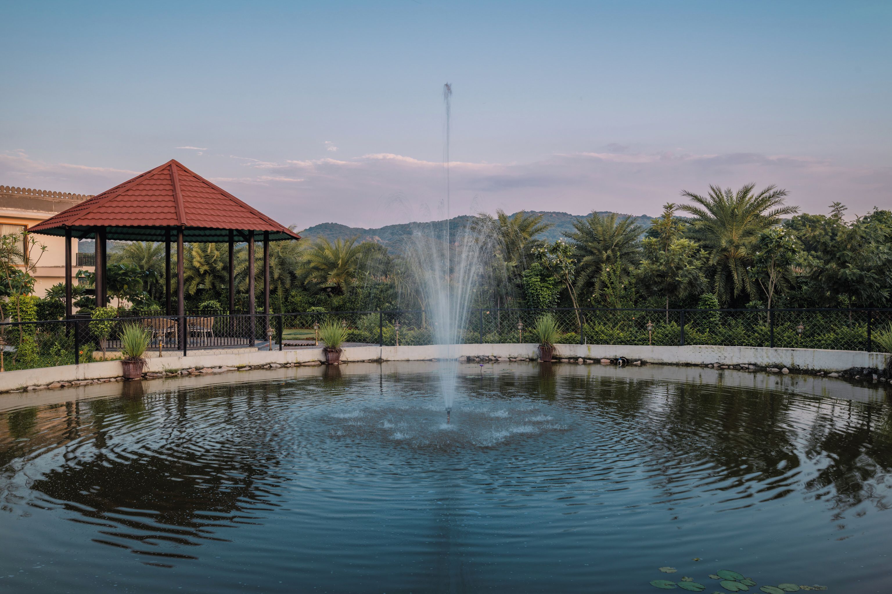 Un étang paisible avec une fontaine, entouré d’une végétation luxuriante et agrémenté d’un belvédère.