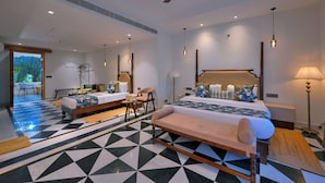 A spacious bedroom with a large bed, a smaller bed, and a bench. There is a ceiling fan, a desk with a chair, and a lamp. The floor has a geometric tile pattern.