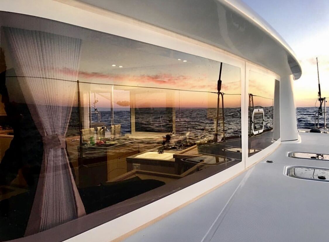 A modern yacht interior with a large glass window offering a view of the ocean and sunset.