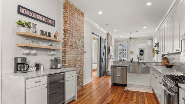 A modern kitchen with white cabinets, a brick accent wall, and wooden flooring.