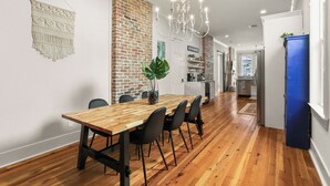 A dining area with a wooden table and chairs, a brick wall, a chandelier, and a blue cabinet.