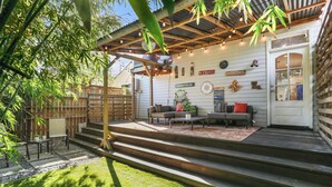 A covered patio with a wooden deck, outdoor seating, and a decorative wall.