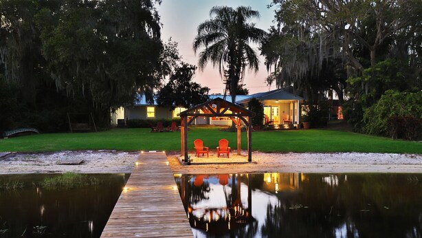 A wooden deck leading to a gazebo with two chairs, a pool, and a house in the background.