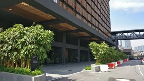 A modern building with a prominent 'EST' sign, large windows, and a covered entrance area with potted plants. - Stazion Services Alila (Kuala Lumpur)