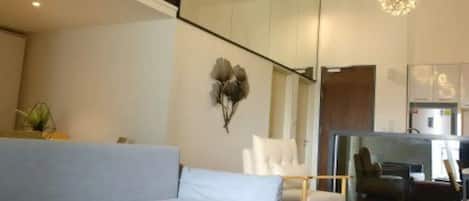 A modern living room with a sofa, a chair, and a small table. There is a decorative wall piece and a ceiling light fixture.