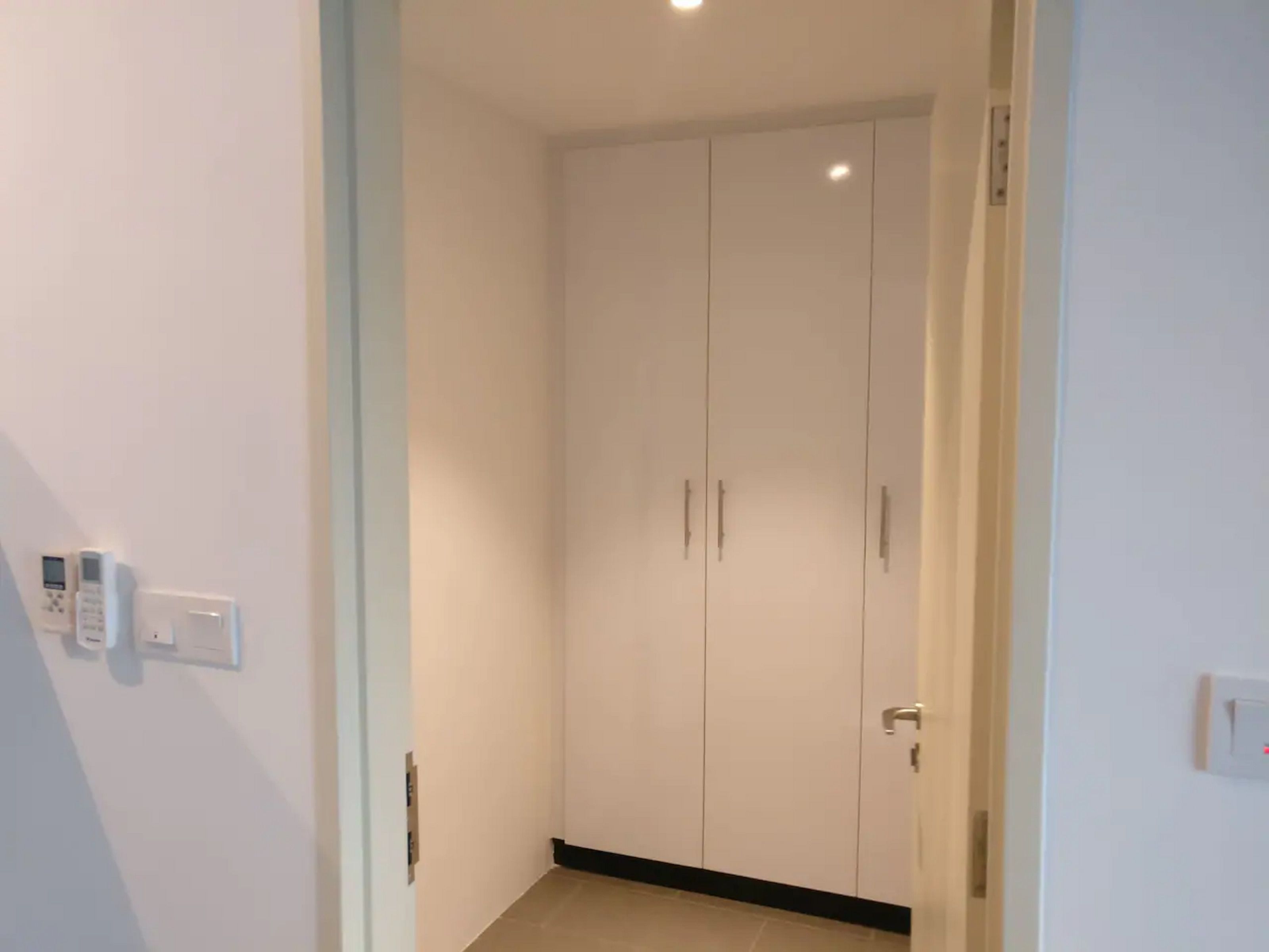 Ein Flur mit einem weißen Kleiderschrank, einem Lichtschalter und einem Thermostat an der Wand.