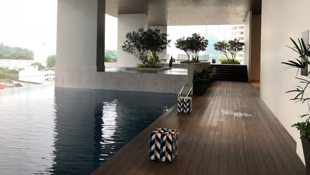 A modern indoor swimming pool with a wooden deck, seating areas, and potted plants. - Stazion Services Alila (Kuala Lumpur)
