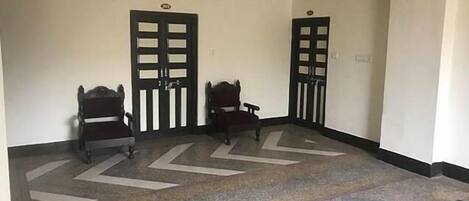 A hallway with two wooden chairs, a clock, and two doors.
