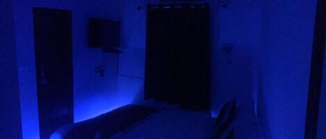 A dimly lit room with a bed, a wall-mounted TV, and a door.