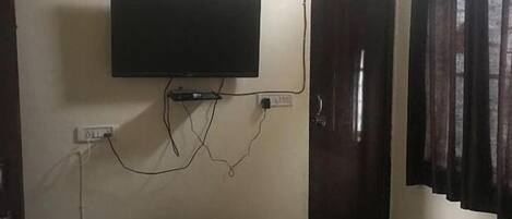 Quarto com televisão na parede, uma porta e cortina.