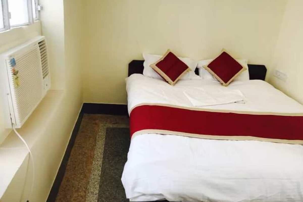 Een klein, netgemaakt bed met een wit en rode dekbedovertrek, twee kussens en een witte radiator aan de muur.