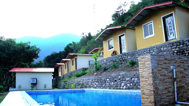 A pool area with a stone wall and a view of houses with red roofs. - Panchvati cottage (Narendranagar)