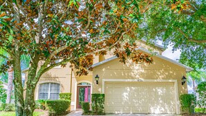A residential house with a garage, a well-maintained lawn, and mature trees. - 7 Beds, 7 Bath Acadia Estates Home with Private Pool and Spa Minutes to Disney! (Kissimmee)