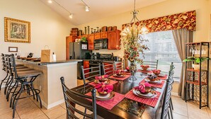 A modern kitchen with a central island, stainless steel appliances, and a dining area with a large table set for six. - 7 Beds, 7 Bath Acadia Estates Home with Private Pool and Spa Minutes to Disney! (Kissimmee)