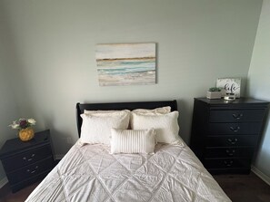 A bedroom with a bed, a nightstand with a vase of flowers, a dresser with drawers, and a wall-mounted painting of a beach scene. - Football Games, A&M Events, Parents Night, etc..our home wins! (College Station)