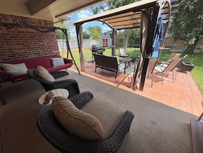 An outdoor patio with wicker furniture, a red sofa, and a covered area with a grill.