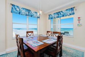 A dining area with a wooden table, four chairs, and a view of the ocean through large windows.