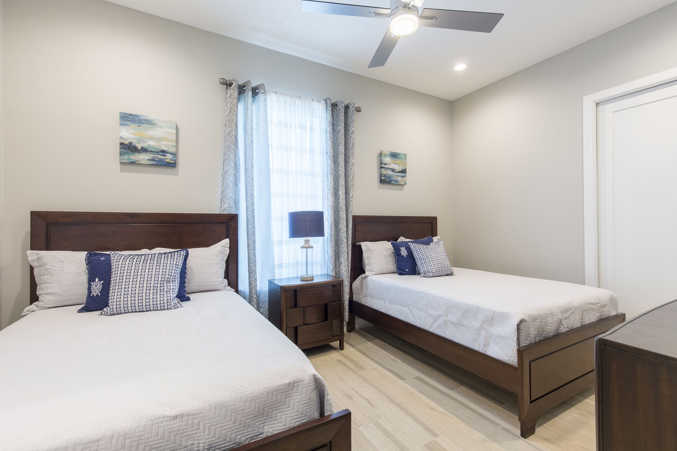 A hotel room with two beds, a ceiling fan, and artwork on the walls.
