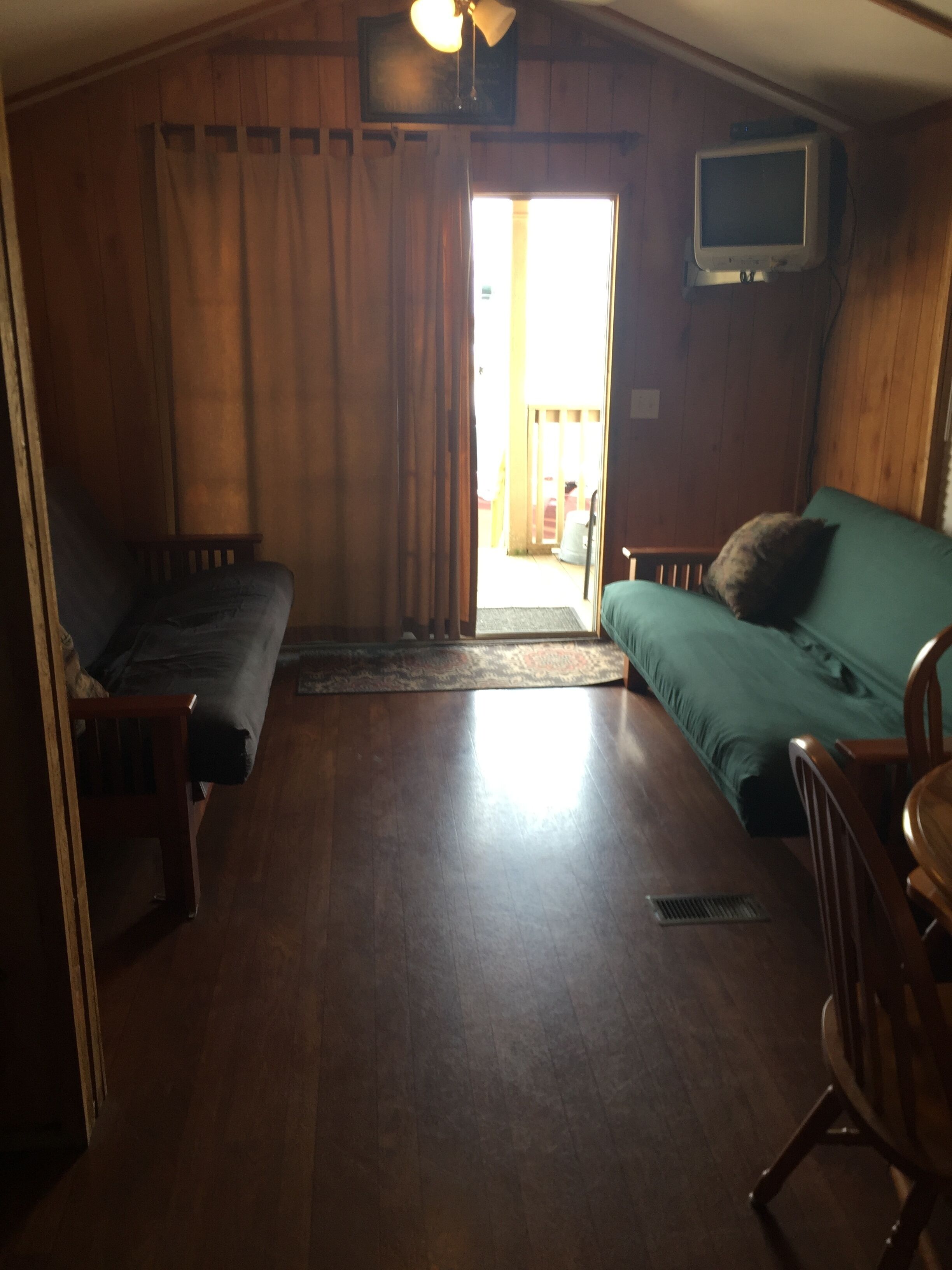 A cozy room with a wooden floor, a green sofa, a wooden chair, a small table, and a television mounted on the wall.