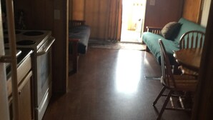 A compact kitchen with a microwave, stove, and wooden cabinets. There is a dining area with a table and chairs, and a television mounted on the wall.