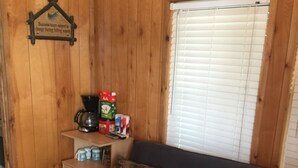 A wooden cabin interior with a sofa, a coffee maker, and a sign indicating business hours subject to change during the fishing season.