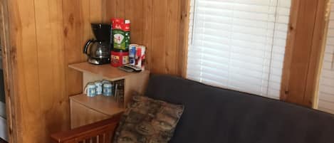 A wooden cabin interior with a sofa, a coffee maker, and a sign indicating business hours subject to change during the fishing season.