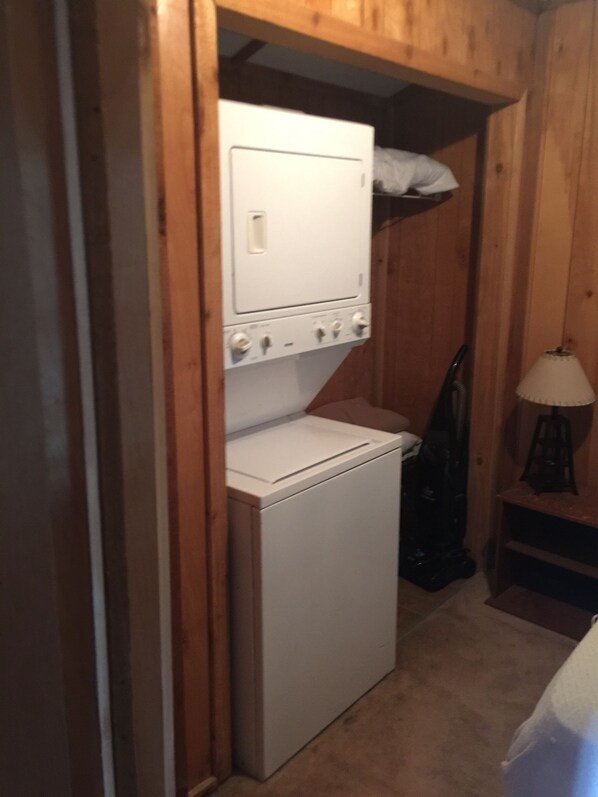 A compact laundry room with a white washer and dryer, wooden walls, and a vacuum cleaner. - "Clean/Maintained Fully Furnished Lodging"-Redfish (Buras)