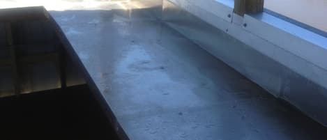 Een kamer met een betonnen vloer, een houten bank en een raam met uitzicht op een veld en een waterpartij.