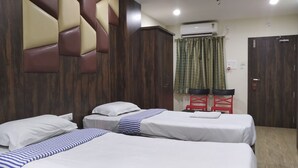 A hotel room with two single beds, a wooden headboard, a wardrobe, and a desk with chairs. - Hotel Bikram (Tezpur)