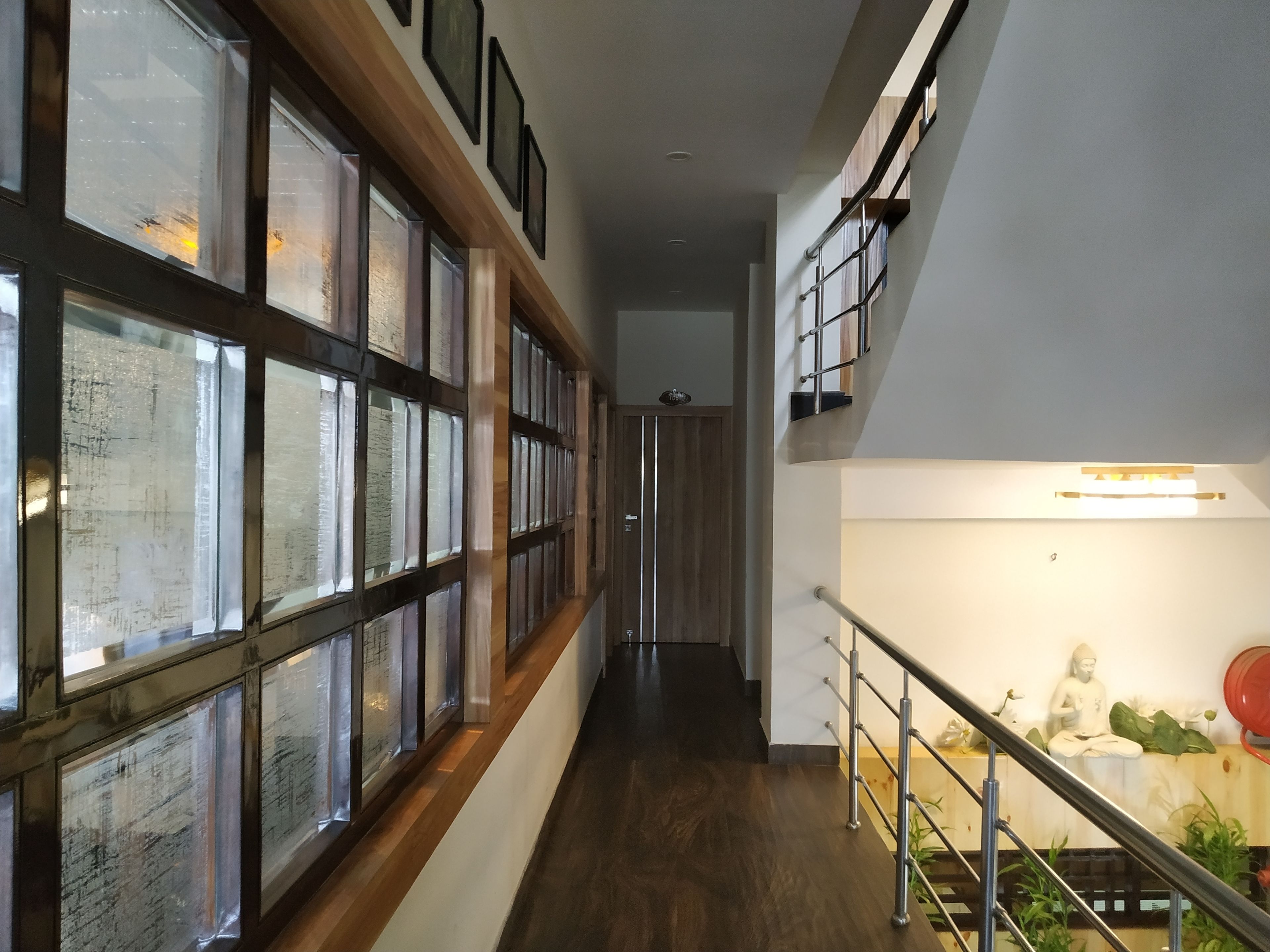 A hallway with wooden flooring, large windows with frosted glass, and a staircase with a railing.