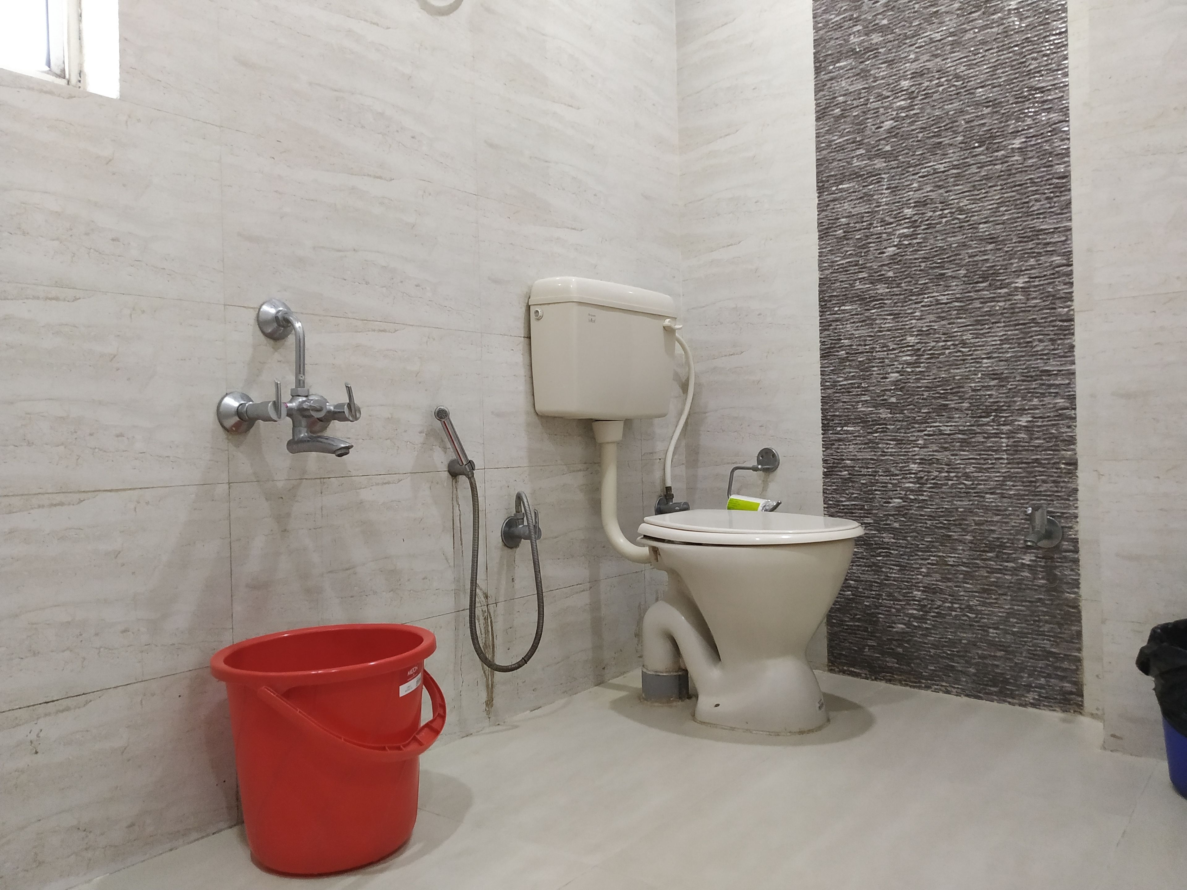 A bathroom with a toilet, a red bucket, and a shower.