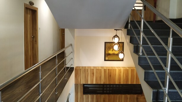 A modern staircase with a metal railing, wooden paneling, and a wall-mounted light fixture. - Hotel Bikram (Tezpur)
