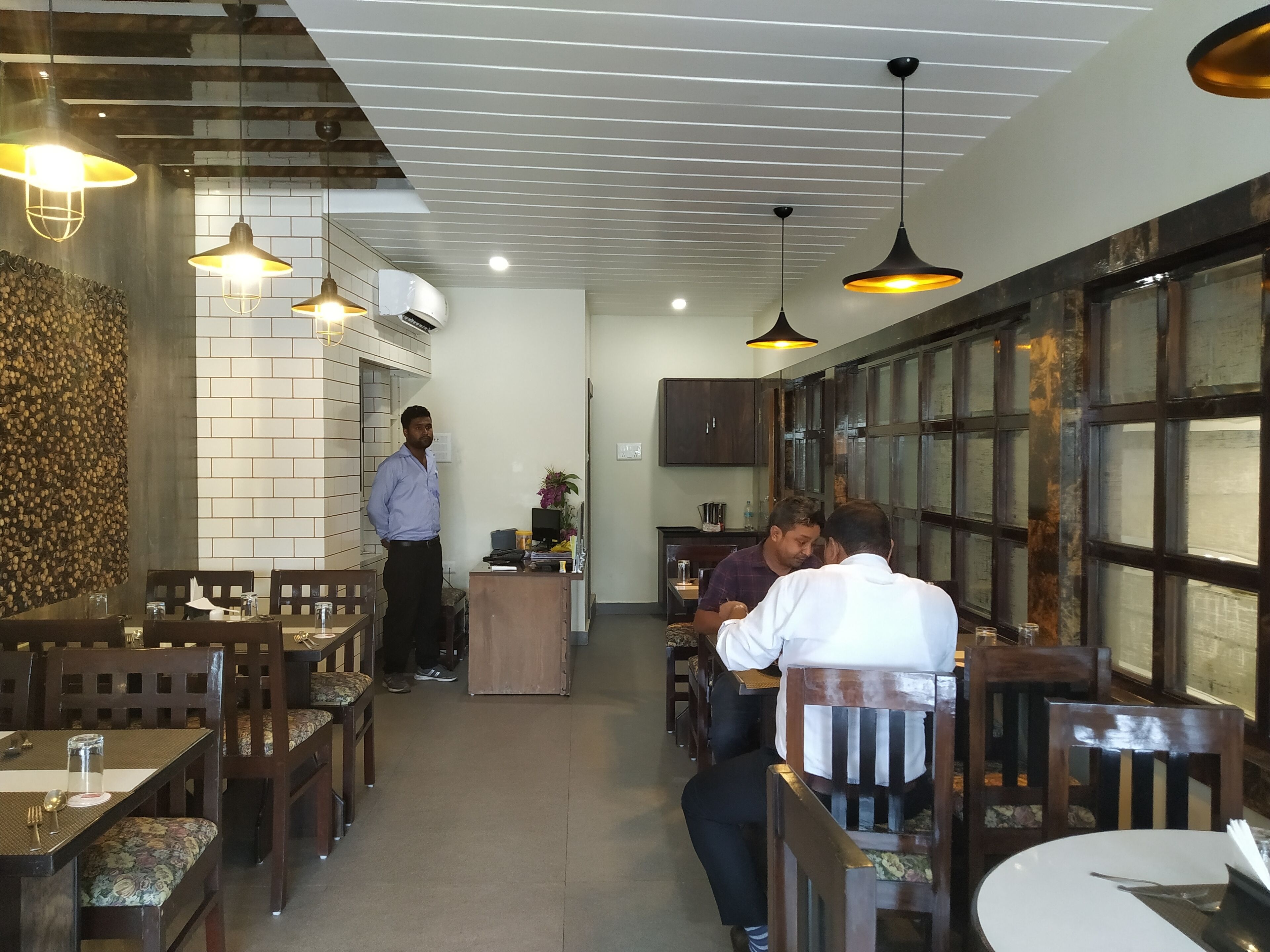 L’intérieur d’un restaurant est décoré de meubles en bois, de luminaires suspendus et d’un mur en briques.