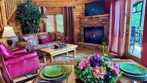 L’intérieur d’un chalet accueillant, avec une cheminée, des murs en bois, un canapé et une table à manger mise avec des assiettes et un verre.