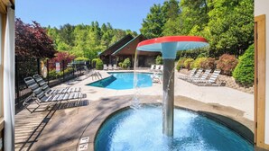 Un espace piscine agrémenté d’un élément décoratif aquatique, de chaises longues et d’un bâtiment en arrière-plan.