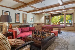 A cozy lounge area with a pool table, a red sofa, and a chess table.