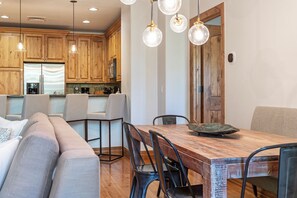 A modern kitchen with wooden cabinets, a dining area with a wooden table and metal chairs, and pendant lights.