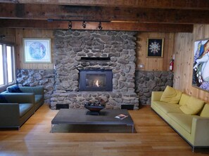 A cozy living room with a stone fireplace, wooden beams, and a yellow sofa. - Mammoth Inn,Queen open shower G (Mammoth Lakes)