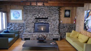 A cozy living room with a stone fireplace, wooden beams, and a yellow sofa. - Mammoth Inn,Queen open shower G (Mammoth Lakes)