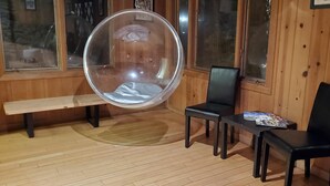 A wooden cabin interior with a large round hanging chair, a bench, and two black chairs. - Mammoth Inn,Queen open shower G (Mammoth Lakes)