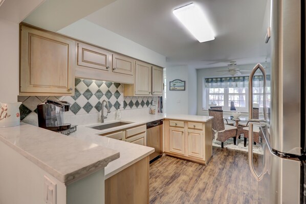 Una cocina con armarios de madera, salpicadero de azulejos y un comedor con sillas de mimbre.