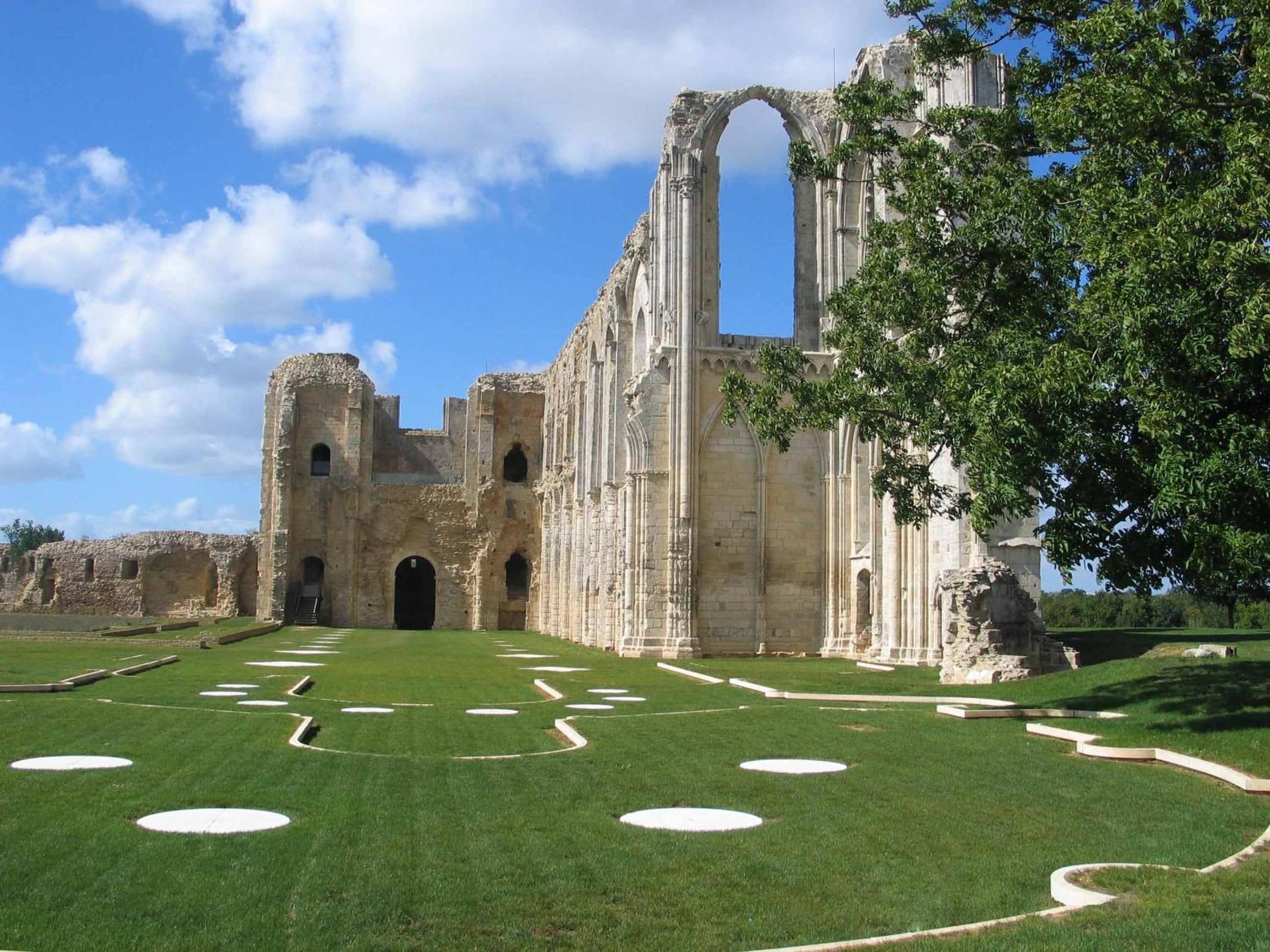 Un edificio histórico de piedra con arcos y columnas, rodeado de un césped bien cuidado con diseños circulares.