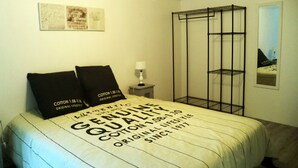 Une chambre à coucher avec un lit, deux oreillers, une table de chevet, une lampe, une étagère en métal noir et un tableau encadré accroché au mur.