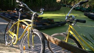 Un vélo jaune est garé sur un quai doté d’une rambarde en bois, entouré de verdure et bordé par une étendue d’eau calme.