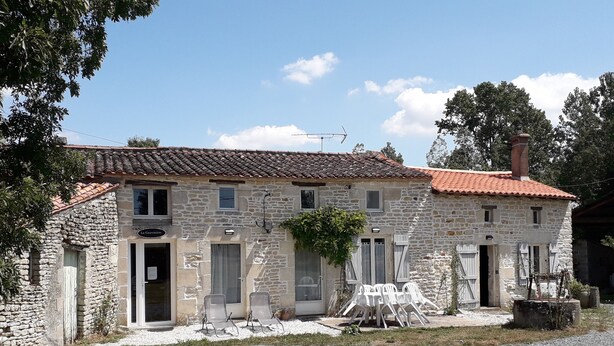 Un bâtiment en pierre avec un toit en tuiles, une allée en gravier et un espace extérieur aménagé pour s’asseoir.