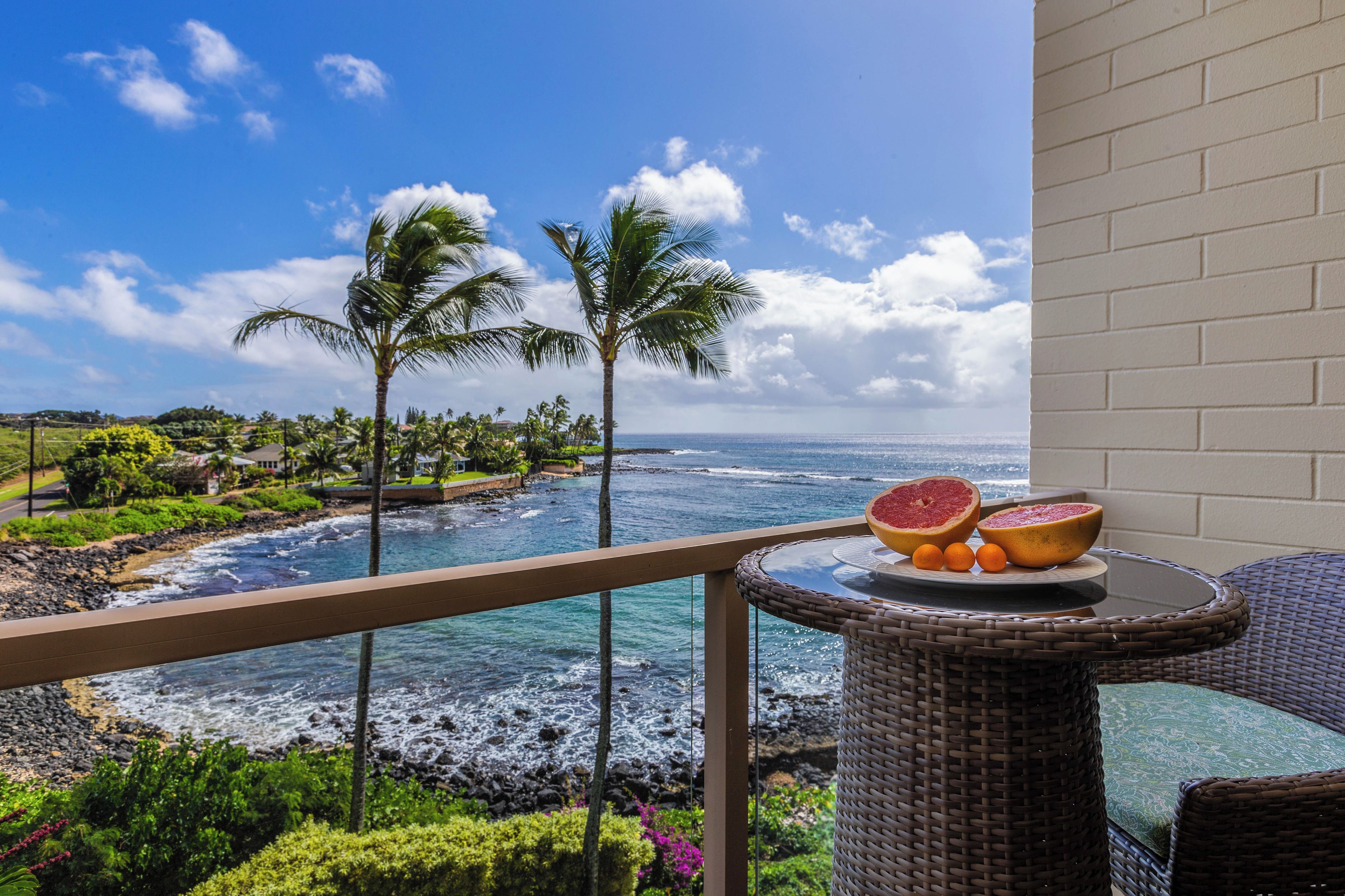 A balcony with a view of the ocean, palm trees, and a table with fruit.