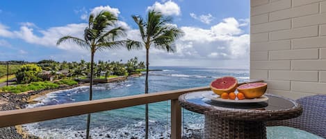 Un balcón con vista al océano, palmeras y una mesa con fruta.