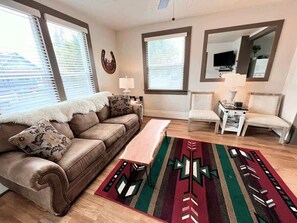 A living room with a brown leather sofa, a wooden bench, a patterned rug, and a small white side table. - Walker's Place, Historic Home, Downtown Whitefish! (Whitefish)