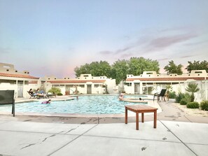 A swimming pool with lounge chairs and a table, surrounded by buildings with a tiled roof.